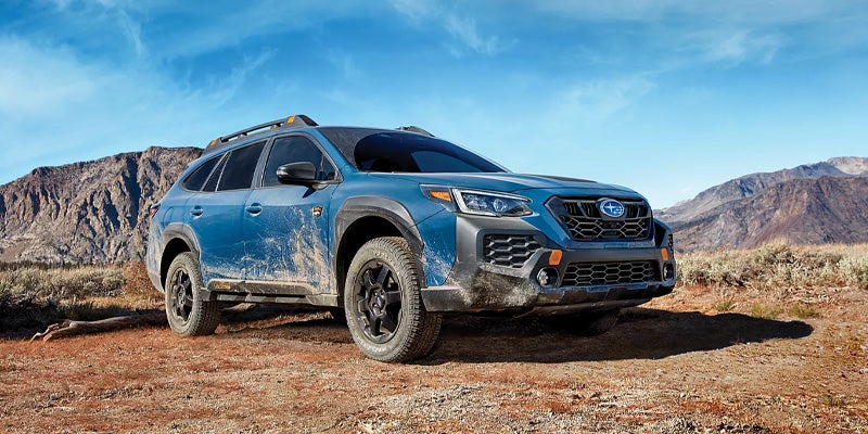 Blue Subaru Outback parked on a rocky desert trail with mountains in the background.